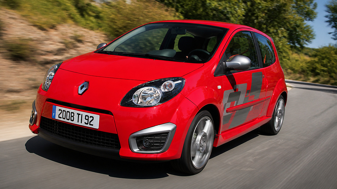 Carro compacto vermelho da Renault em movimento em estrada com vegetação ao fundo.