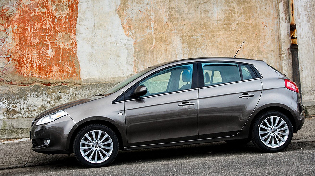 Carro hatchback cinza estacionado ao lado de parede antiga com pintura descascada.
